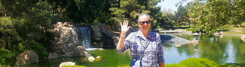 Alumna Kristie Koepplin stands in CSULB's Earl Burns Miller Japanese Garden and waves at the camera.